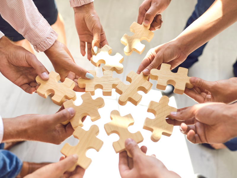 Hands holding puzzle pieces, coming together.